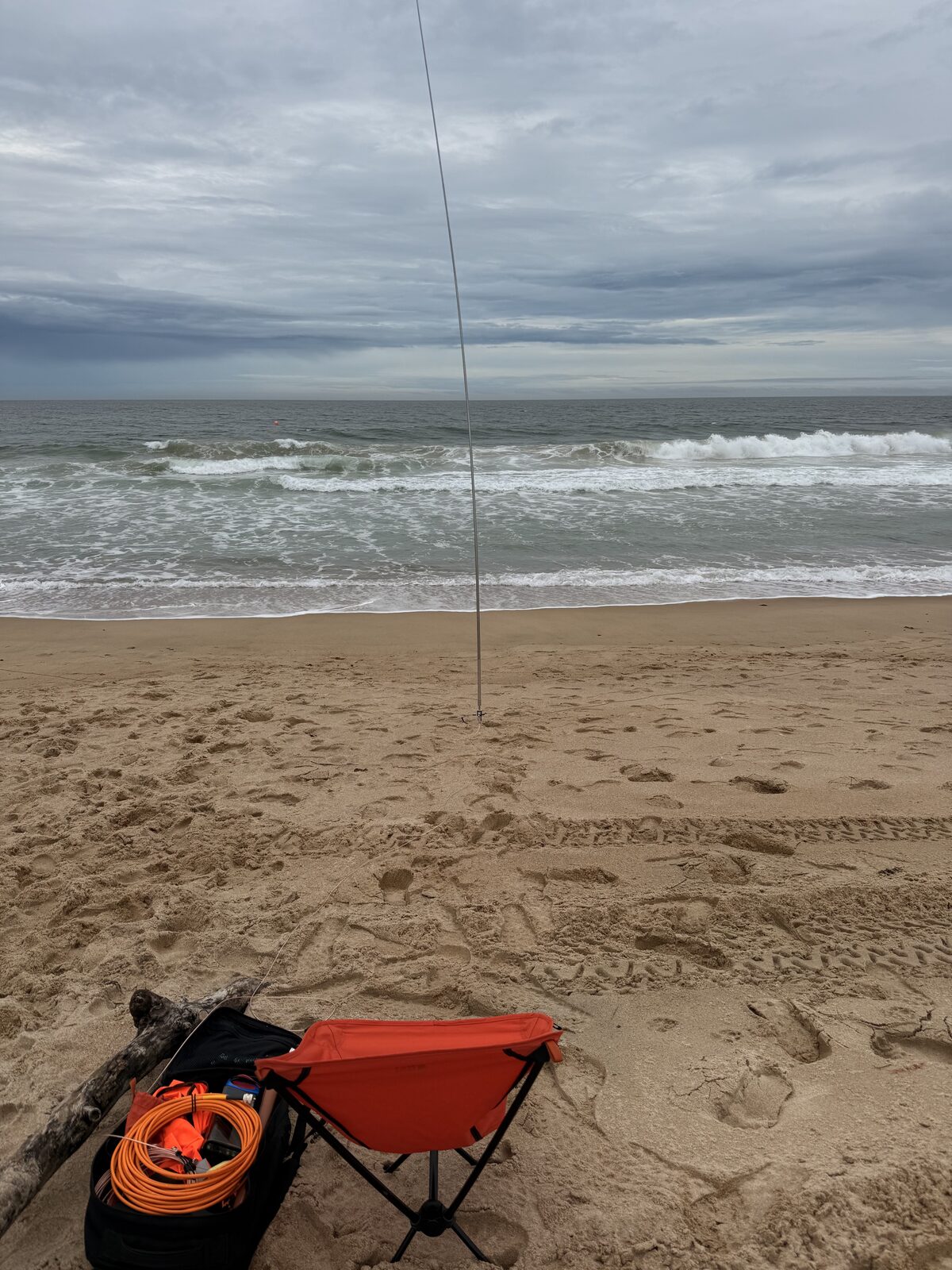 Beach chair, pack, and vertical whip looking out over the overcast surf
